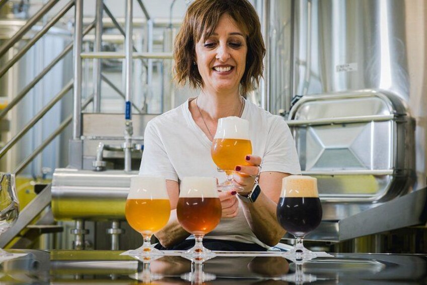 A person holding three glasses of beer in a brewery setting. 4