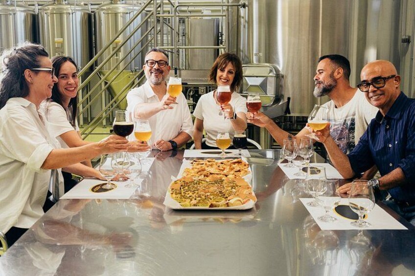 A group of people toasting with drinks around a table with a pizza. 1