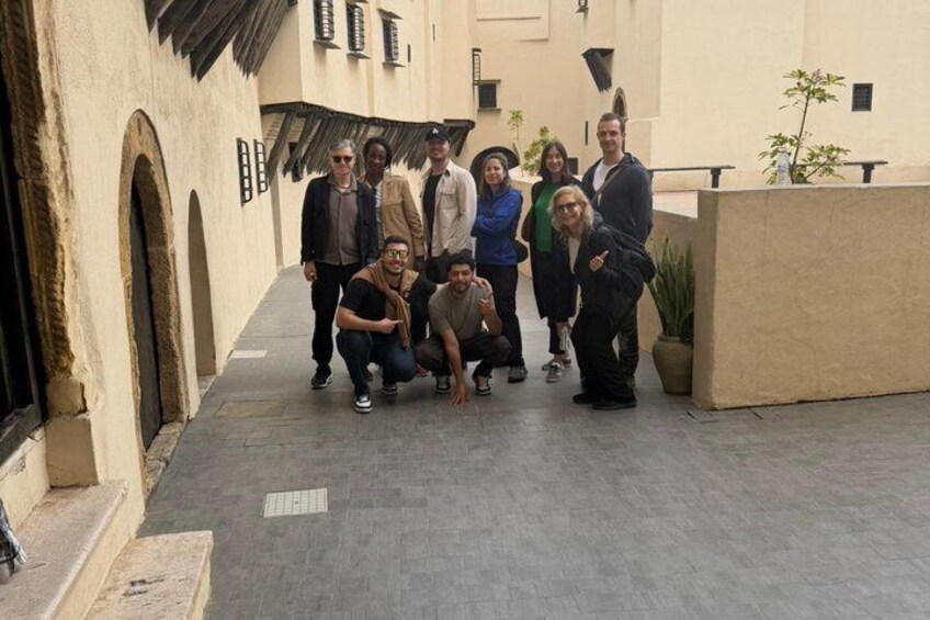 A group of people standing in an outdoor courtyard with arches and potted plants. 1