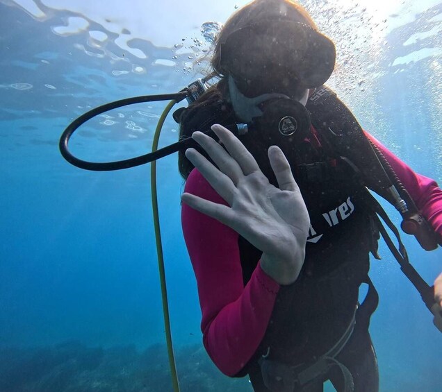 A person scuba diving underwater with a black wetsuit and pink long-sleeve shirt, holding onto a metal rail. 2