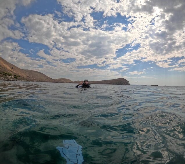 A person swimming in clear blue water with a mountainous landscape in the background. 2