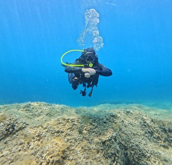 A diver underwater with a yellow hose, surrounded by a rocky seabed. 1