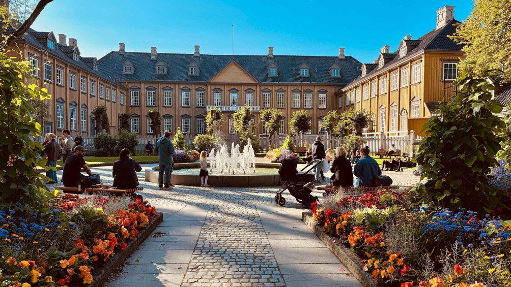 A courtyard with a fountain, people sitting and walking, and a building with a tiled roof in the background. 3