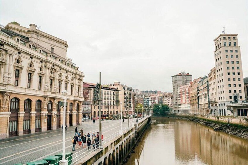 A river with buildings on both sides, a bridge, and people walking. 2