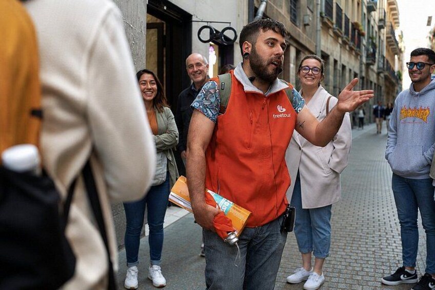 A person in an orange vest gesturing, with a backpack and a booklet. 1