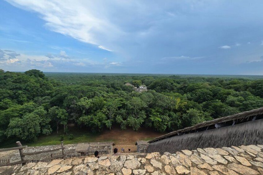 A stone structure with a view of a dense forest and a distant building. 2