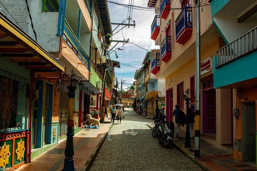 A cobblestone street lined with colorful buildings, a motorcycle parked on the right, and a few pedestrians in the distance. 4