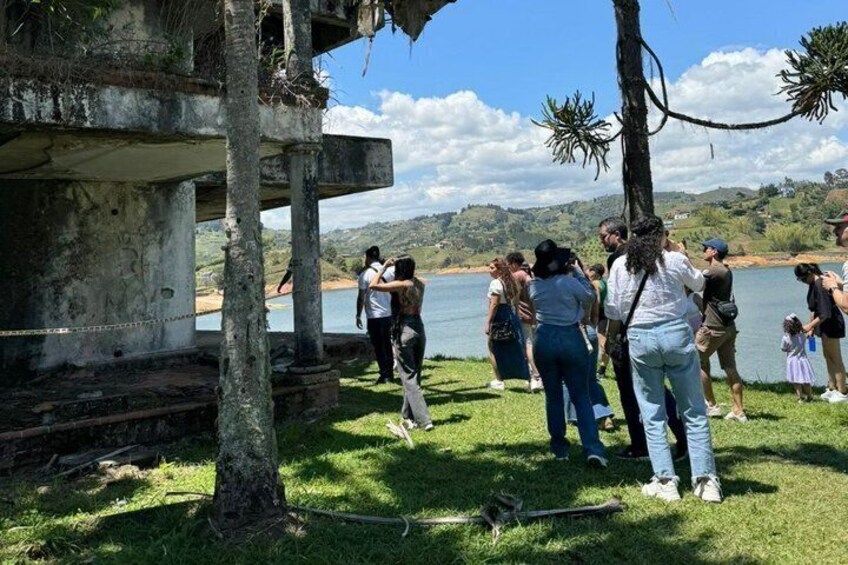 A group of people standing near a historical structure by a lake with a clear sky. 3