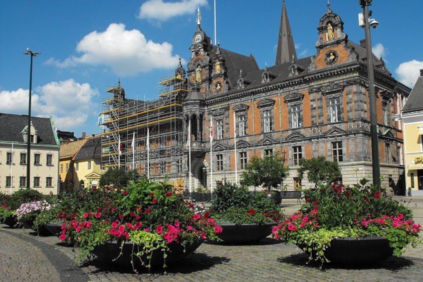 A historic building with scaffolding, surrounded by flower beds with pink flowers. 1