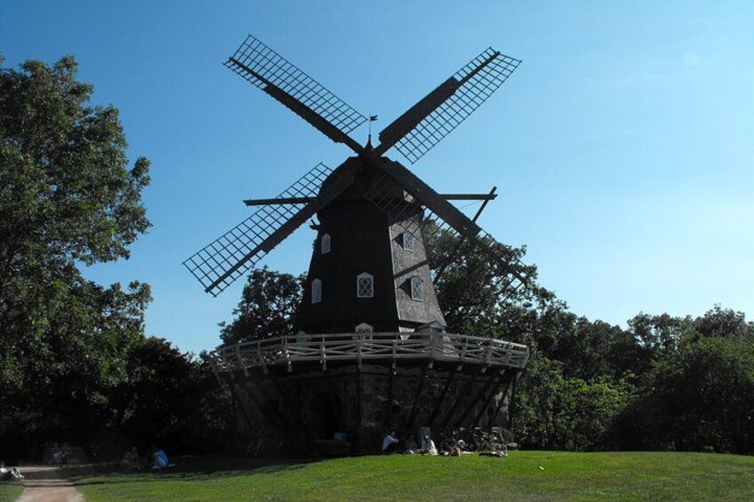 A traditional windmill with a large, open structure and a surrounding grassy area. 3
