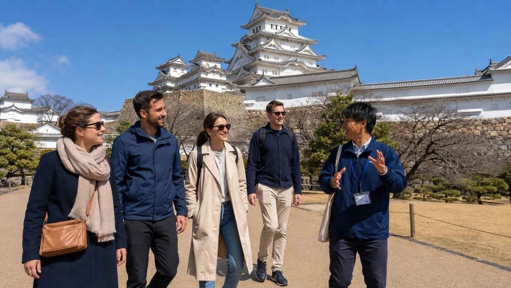 A group of people walking in front of a traditional Japanese castle with multiple tiers and white walls. 1