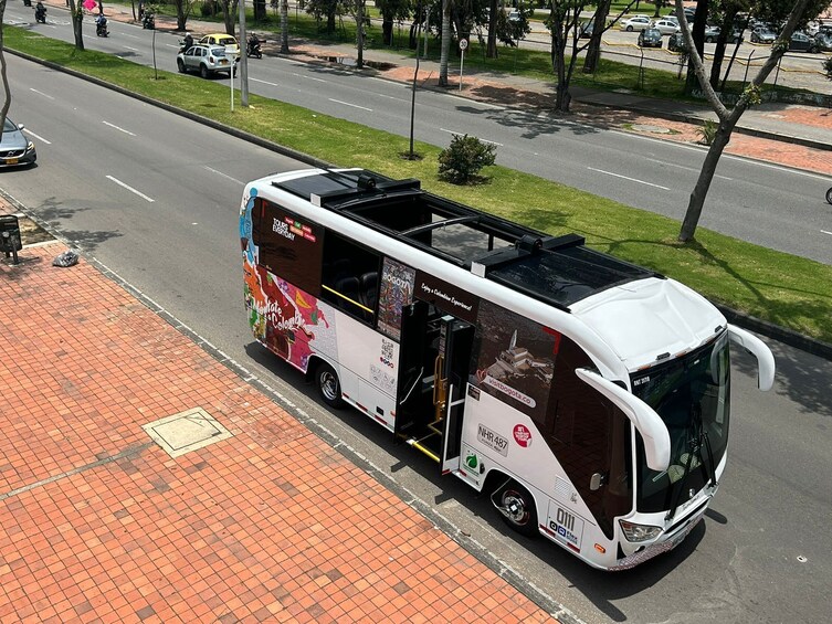 En vit turistbuss med färgstarka reklamtryck parkerad på en röd tegelbelagd trottoar. 2