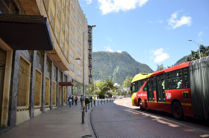 En gata med en röd buss, en byggnad med en skylt där det står ”Continental”, och ett berg i bakgrunden. 1