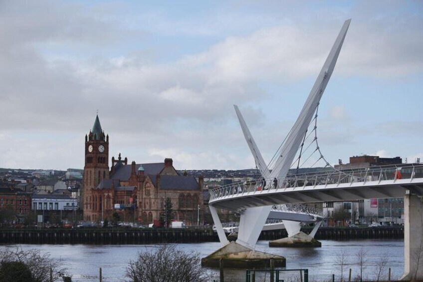 A modern bridge with a unique design, a historic building with a clock tower, and a river in the foreground. 1