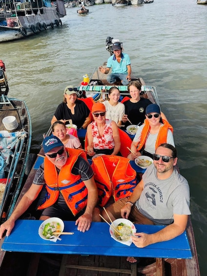 A group of people on a boat with life jackets, eating noodles. 3