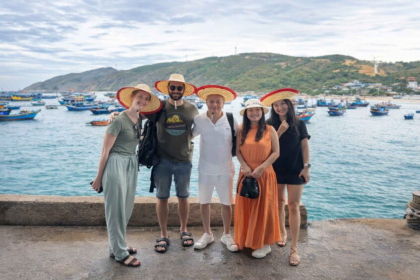 A group of people standing by a waterfront with boats and wind turbines in the background. 1