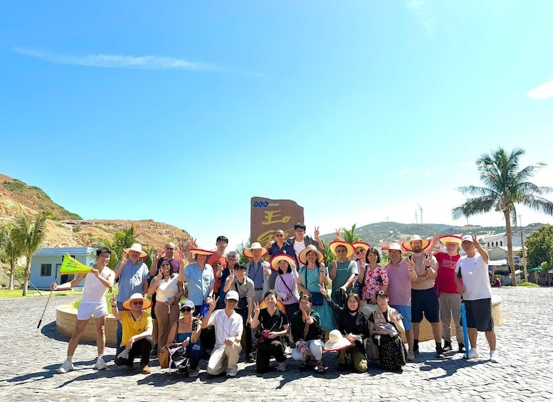 A group of people posing for a photo in a sunny outdoor setting with a clear sky, palm trees, and a sign with a symbol. 3