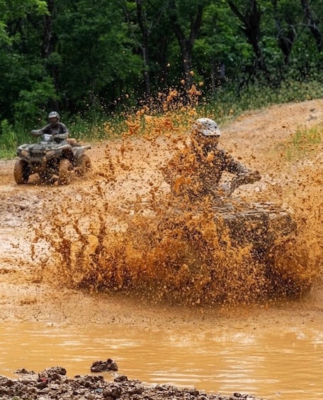 A person riding an ATV through a muddy area, splashing mud. 1
