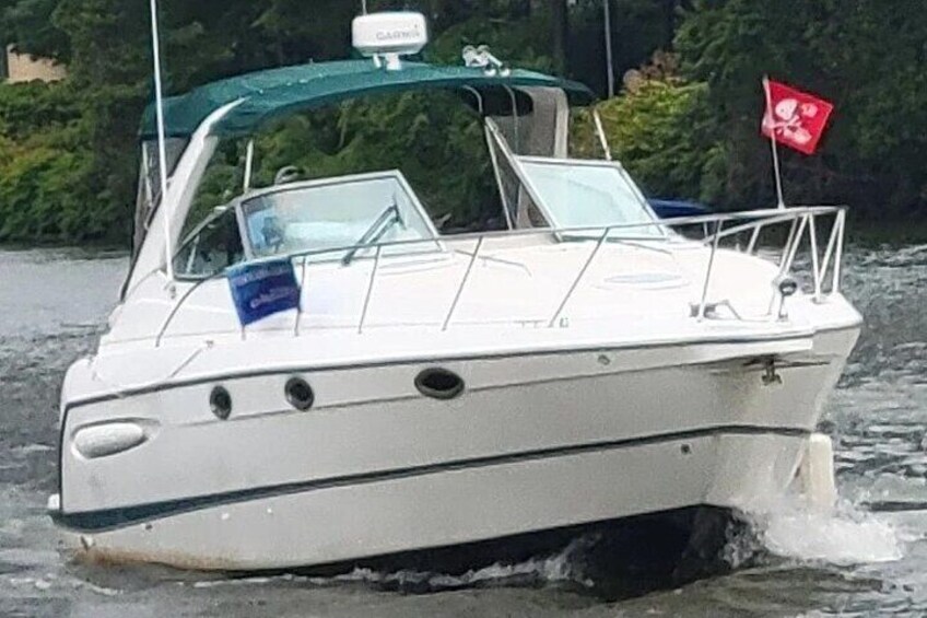A white boat with a blue flag, moving through water with a red flag in the background. 1