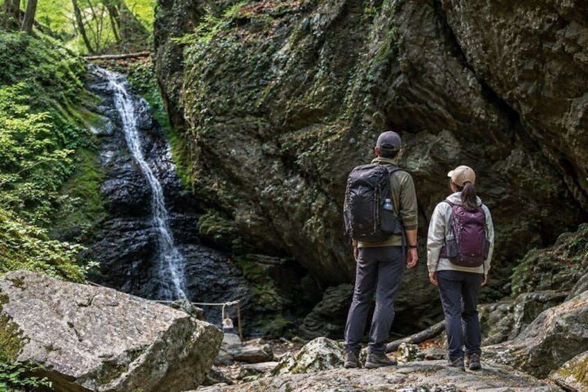 Two hikers on a rocky trail with a waterfall in the background. 5