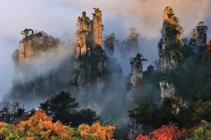 A misty mountain landscape with towering rock formations and autumn-colored trees. 1
