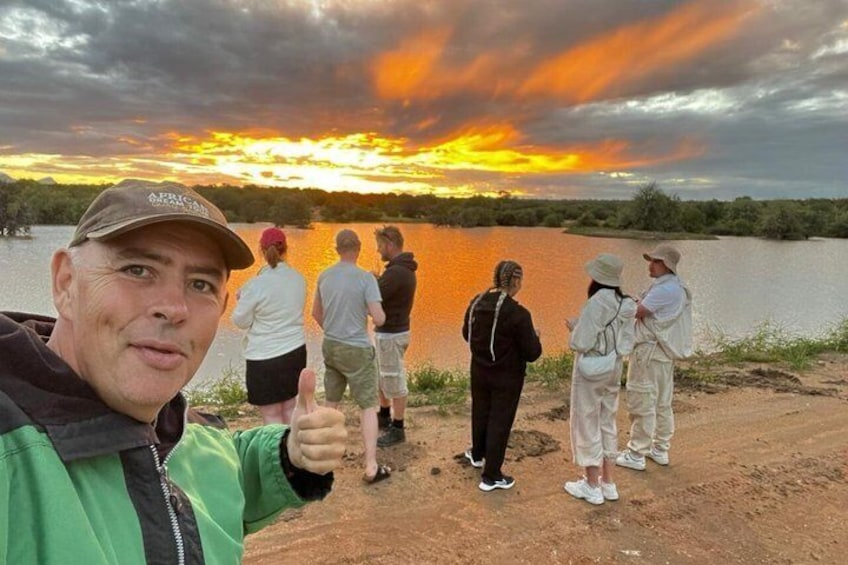 A group of people standing by a body of water during sunset. 1