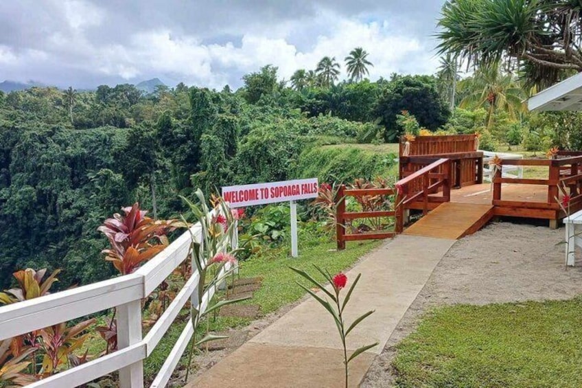 A sign welcoming visitors to Sopoaga Falls, surrounded by lush greenery and a wooden walkway. 4