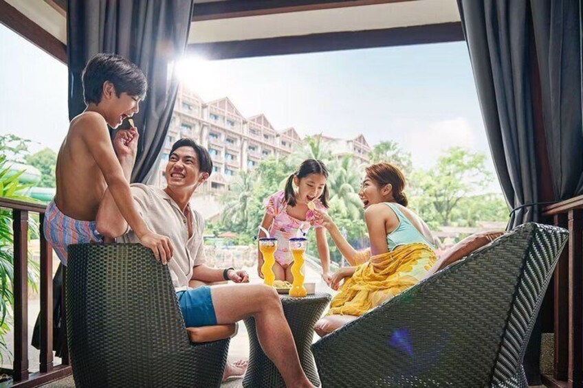 A group of people sitting on wicker chairs on a balcony with a view of a resort and palm trees. 2