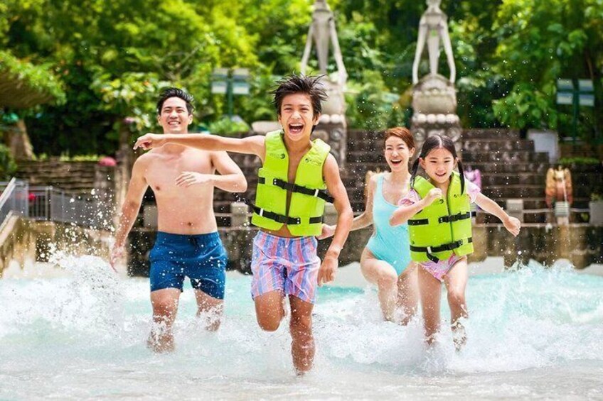 People running in water, wearing life jackets, with a fountain and greenery in the background. 1