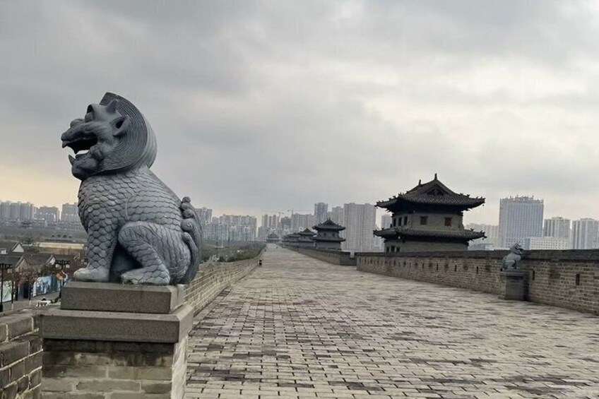 A stone lion statue on a paved pathway, traditional Chinese architecture in the background, and a cityscape with modern buildings. 2