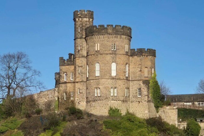 A large, historic stone castle with multiple towers and battlements, surrounded by greenery and a clear sky. 2