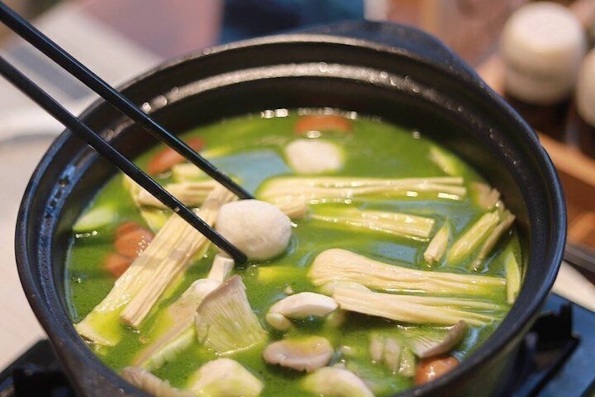 A pot of soup with chopsticks, containing vegetables and a dumpling. 3