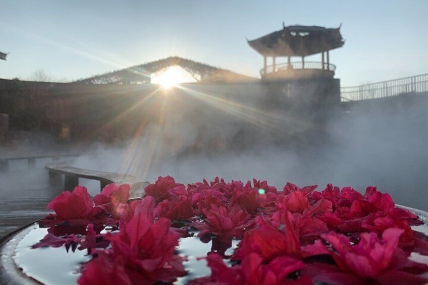 A hot spring with red flowers in the foreground and a traditional pavilion in the background. 1