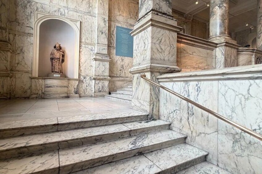 Marble steps leading to a statue, with columns and a plaque in a grand hall. 5