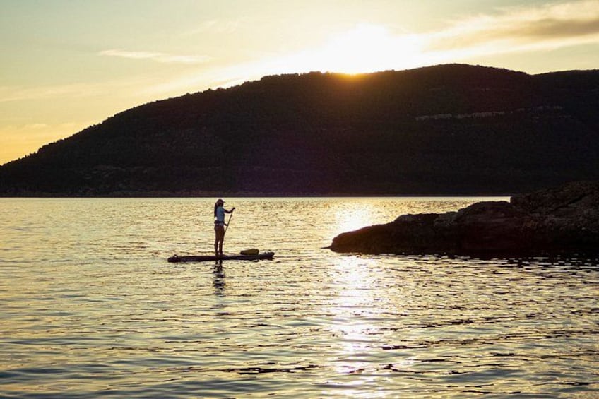 A person paddleboarding on calm water during sunset with a mountain in the background. 4