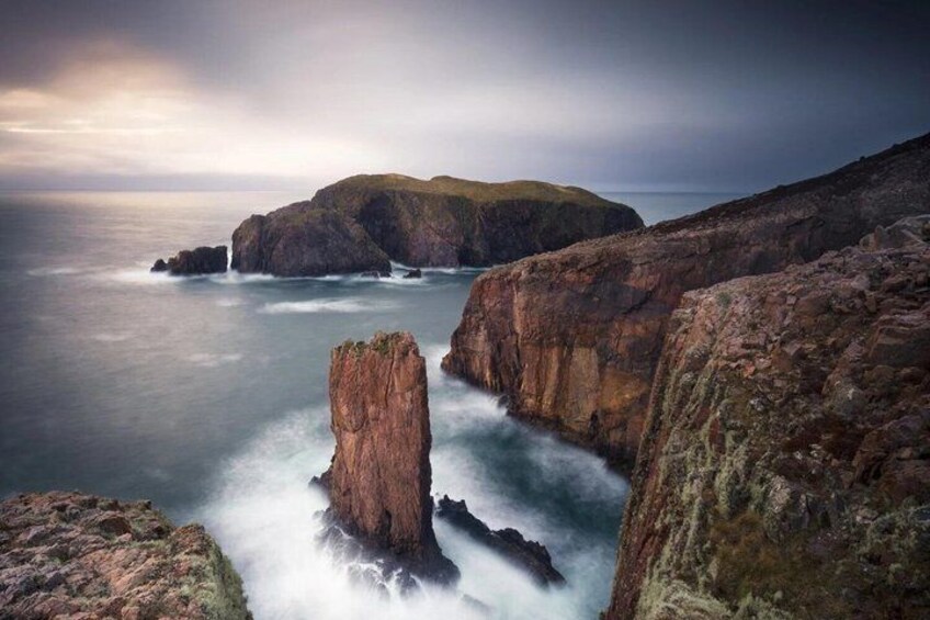 A coastal landscape with rocky cliffs, a prominent rock formation, and the ocean. 5