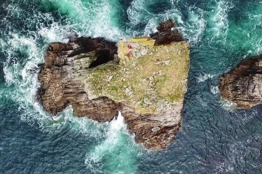 An aerial view of a rocky island surrounded by turbulent ocean waves. 1