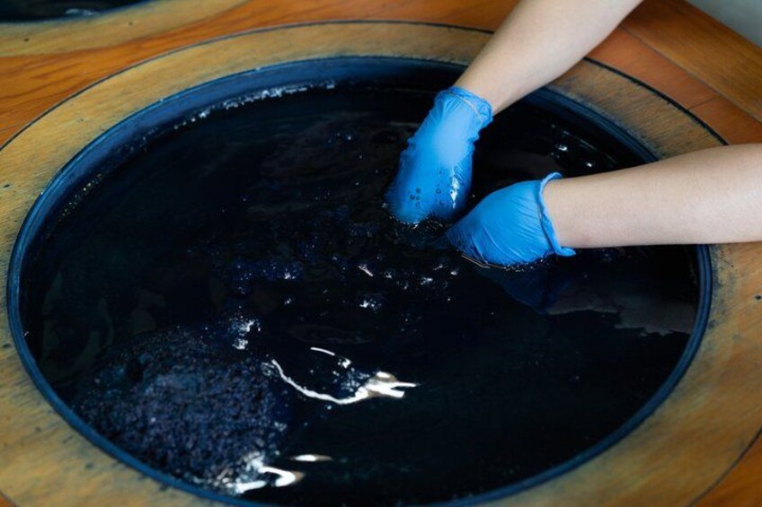 A person wearing blue gloves handling a black liquid in a round container. 1