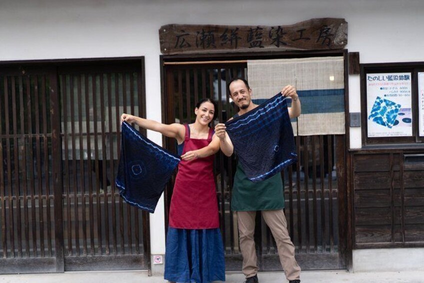 Two people holding a blue fabric, standing in front of a building with a sign. 1