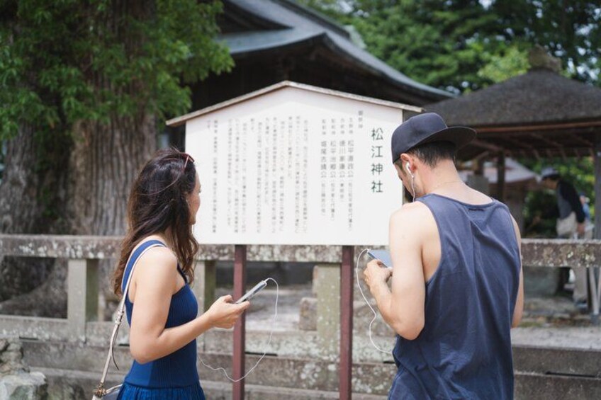 A couple standing in front of a traditional Japanese structure with a signboard. 2
