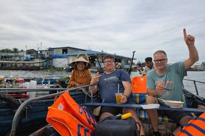 People on a boat with life jackets, a man pointing upwards, and another man holding a drink. 1