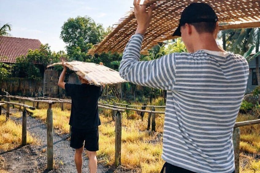 Two people carrying a woven roof structure. 2