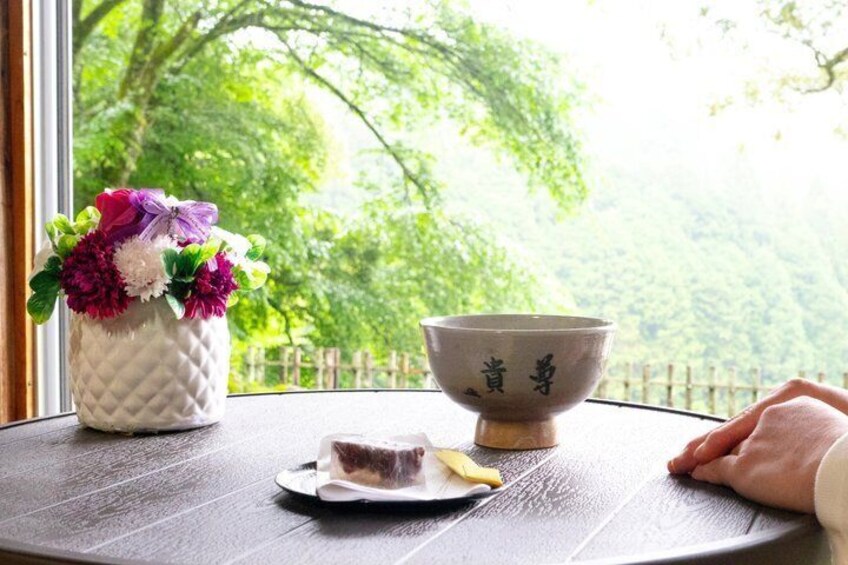 A table with a bowl and a plate of food, a vase with flowers, and a window with a view of trees. 3