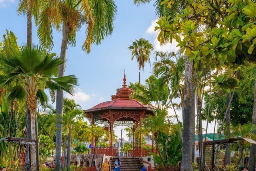 A gazebo with a red roof surrounded by palm trees and greenery. 3