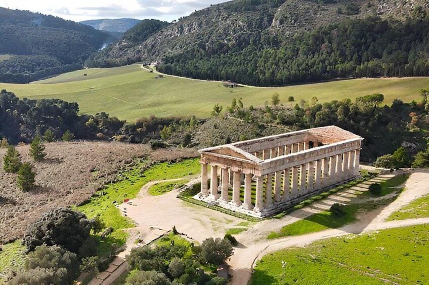 An ancient Greek temple surrounded by lush green fields and hills. 5