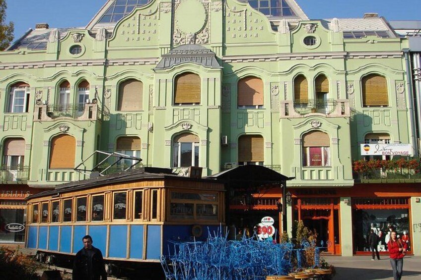 A green building with arched windows and a tram in front. 1