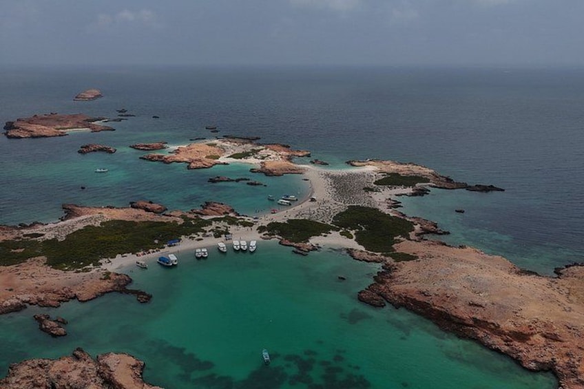 A coastal landscape with clear turquoise waters, rocky formations, and several boats anchored near the shore. 1