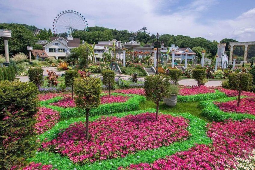 A park with flower beds, a Ferris wheel, and houses in the background. 5