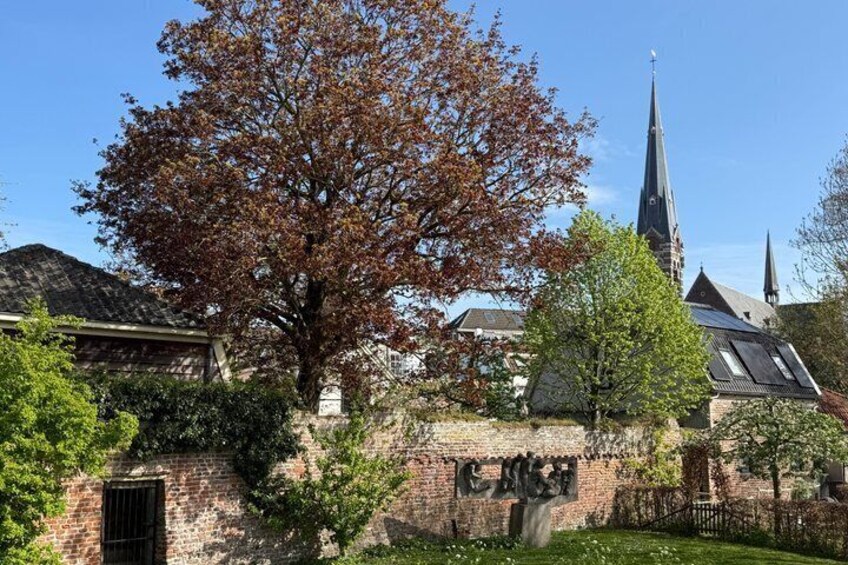 A church with a tall steeple, a brick wall with a gate, and a large tree with autumn leaves. 2