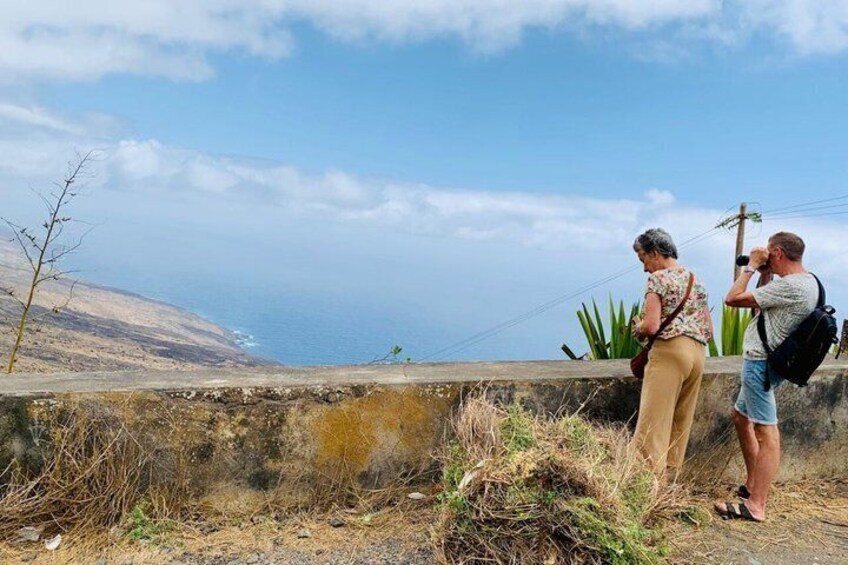 Two people standing on a concrete ledge overlooking a coastal landscape with sparse vegetation and a clear sky. 2